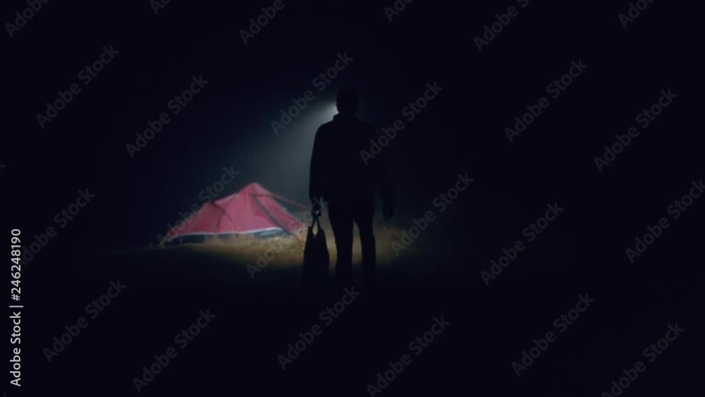 A man wearing a headtorch searches for his tent at night during a storm
