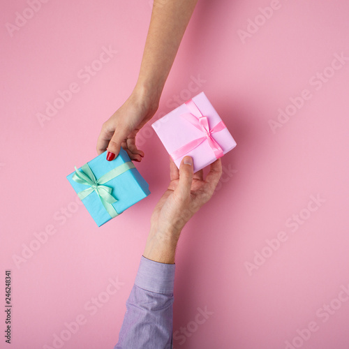 man and girl exchanging gifts from hand to hand,boxes wrapped in decorative paper with a bow on pastel background, the concept of holidays and love , top view