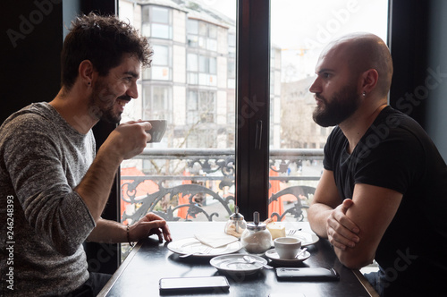 Two young guys with beards drink a coffee and having a nice conversation.