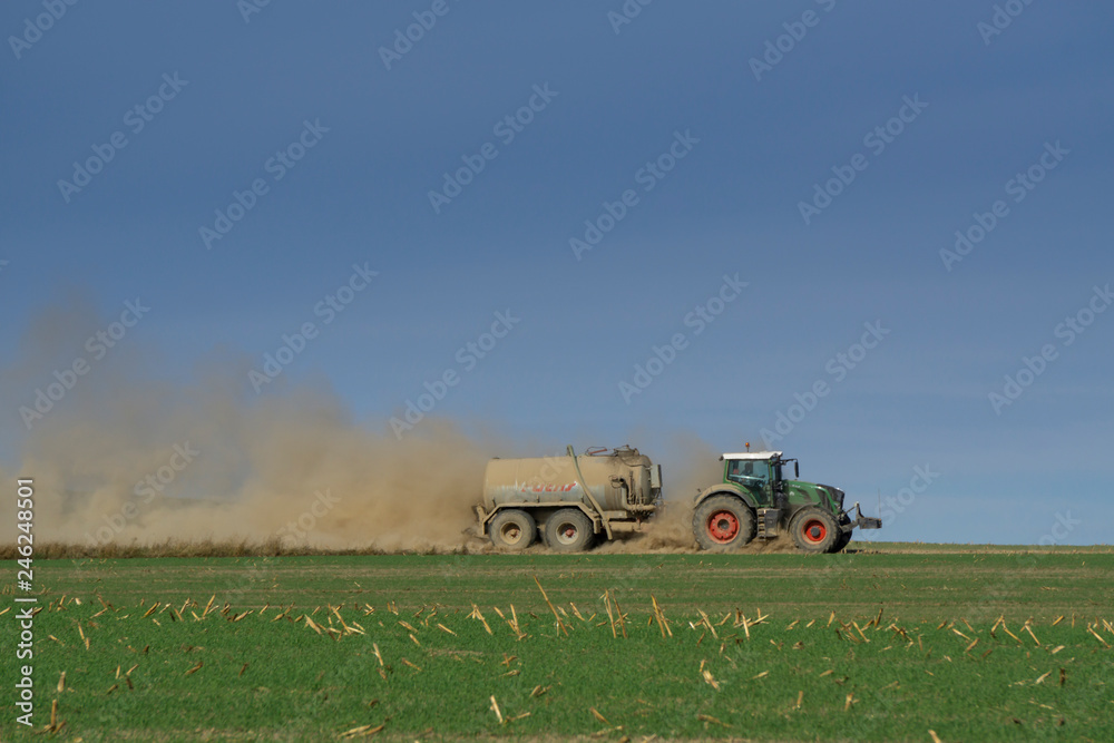 Fototapeta premium tractor with trailer drives across the field and stirs up a lot of dust