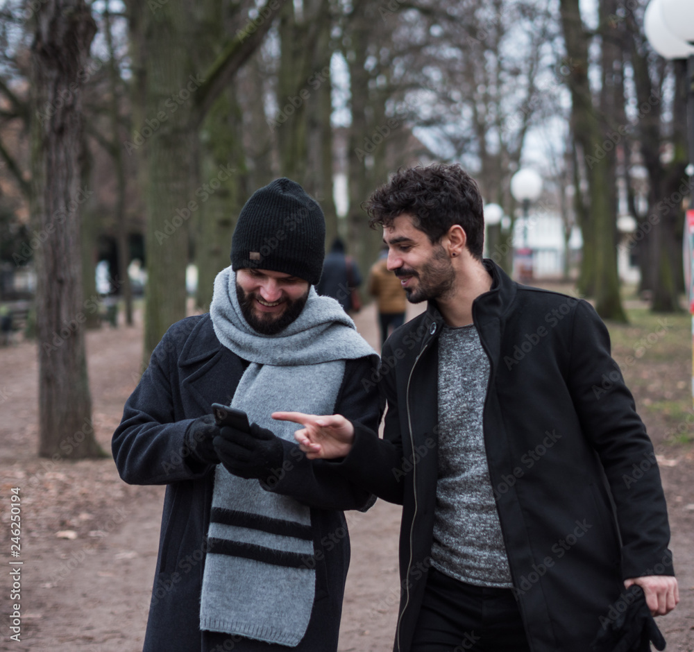 two young guys friends with beards look at the phone while walking in a park two young guys friends with beards look at the phone while walking in a park