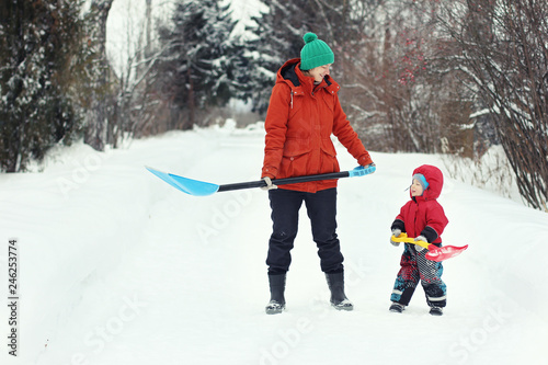 Young mother and her toddler son stand with snow shovels on rural road. Winter seasonal concept © Gargonia