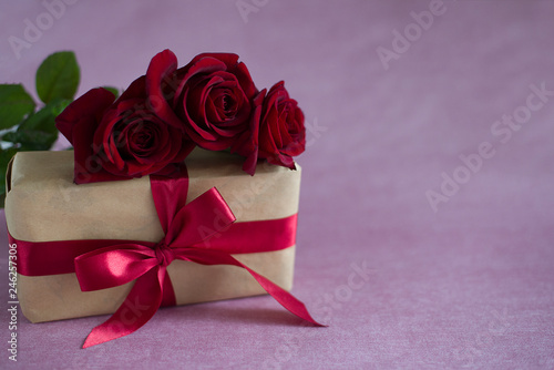 box tied with red ribbon  three red roses on pink background  horizontally  close up 