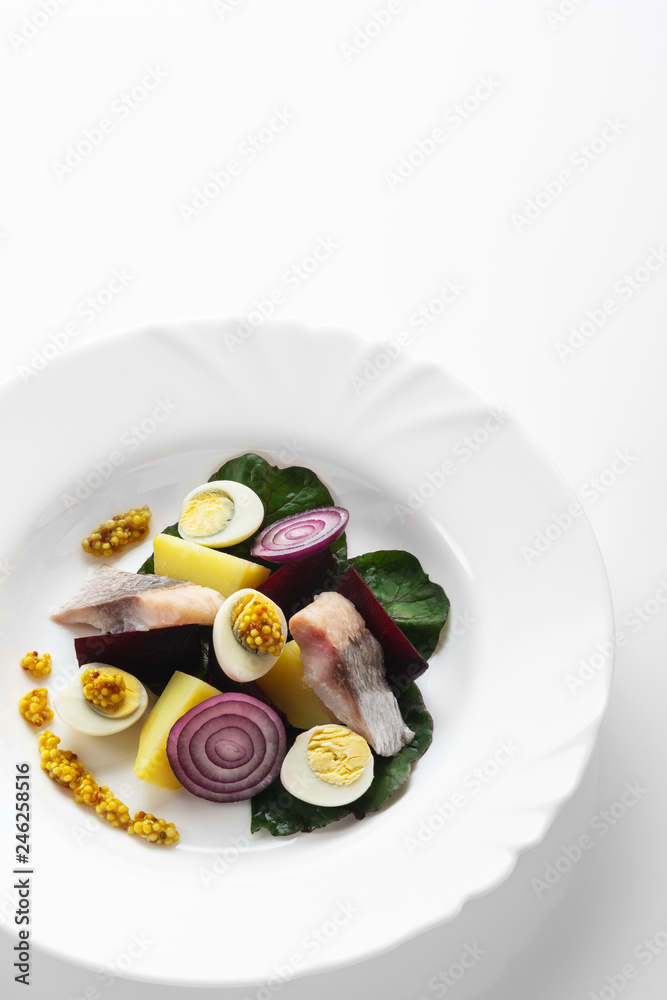 Salad from salty herring, beet, boiled potatoes, quail eggs and onions. With french mustard. High Key. Selective focus.