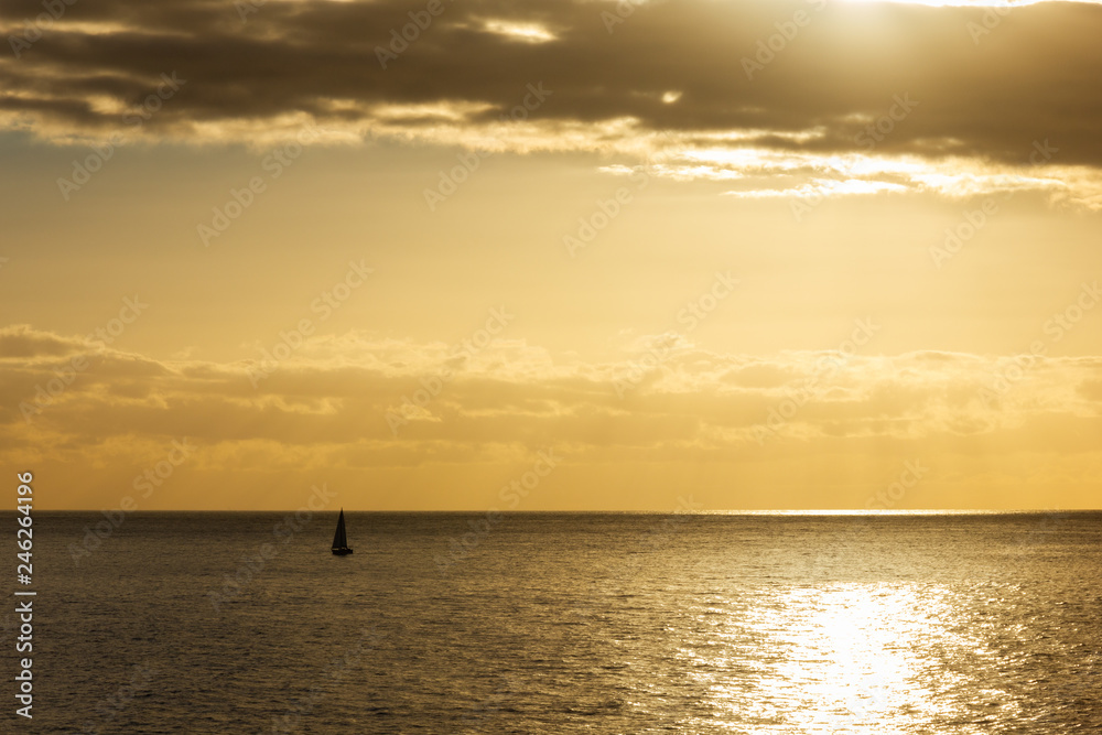 Silhouette of lonely sailboat on big ocean at stunning sunset. Small ship in the middle of sea at twilight. Lost in immensity concept
