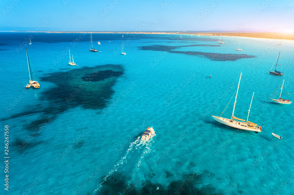 Aerial view of boats and luxury yachts in transparent sea at sunny bright day. Summer seascape. Tropical landscape with lagoon, sailboats, azure water, sandy beach, sky. Top view from drone. Travel