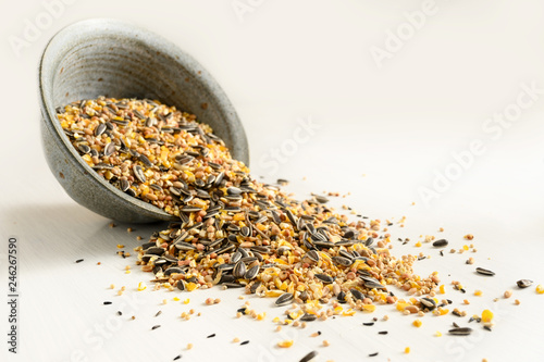 bird food from mixed seeds like sunflower, corn, millet and more, are falling out of a bowl on a light background, copy space