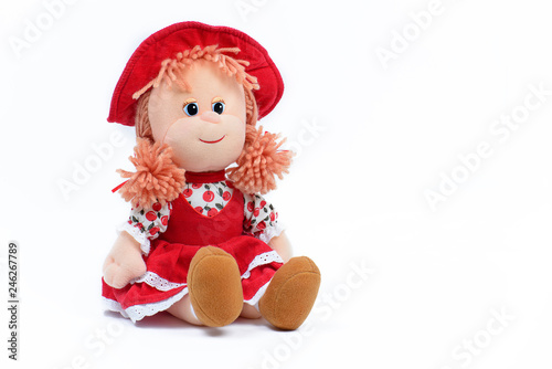 Soft doll in a red dress and hat on a white background. Children's toy. Close-up.