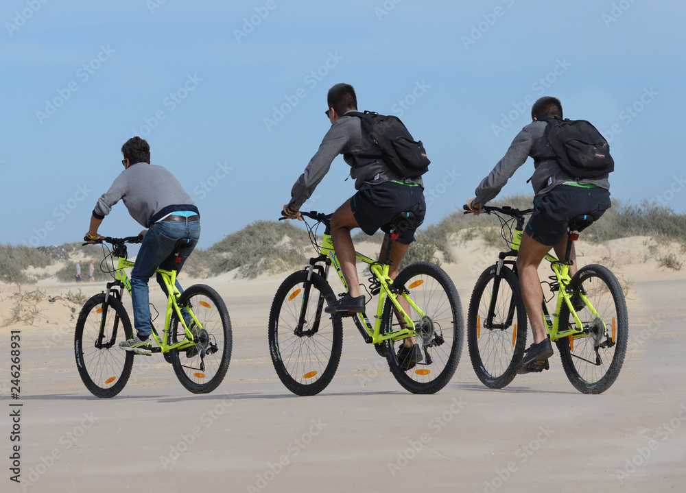 Paseo en bicicleta: 3 ciclistas en el Parque Nacional de Las Dunas de Corralejo, Fuerteventura, Islas Canarias