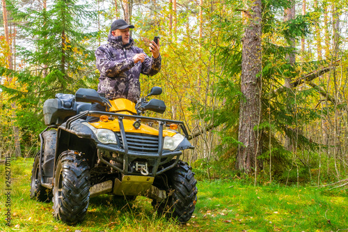  ATV. A man rides through the forest on an all-terrain vehicle. Quad bike. In the woods. Trip to the forest on ATV. The traveler checks the route on the map on the phone.