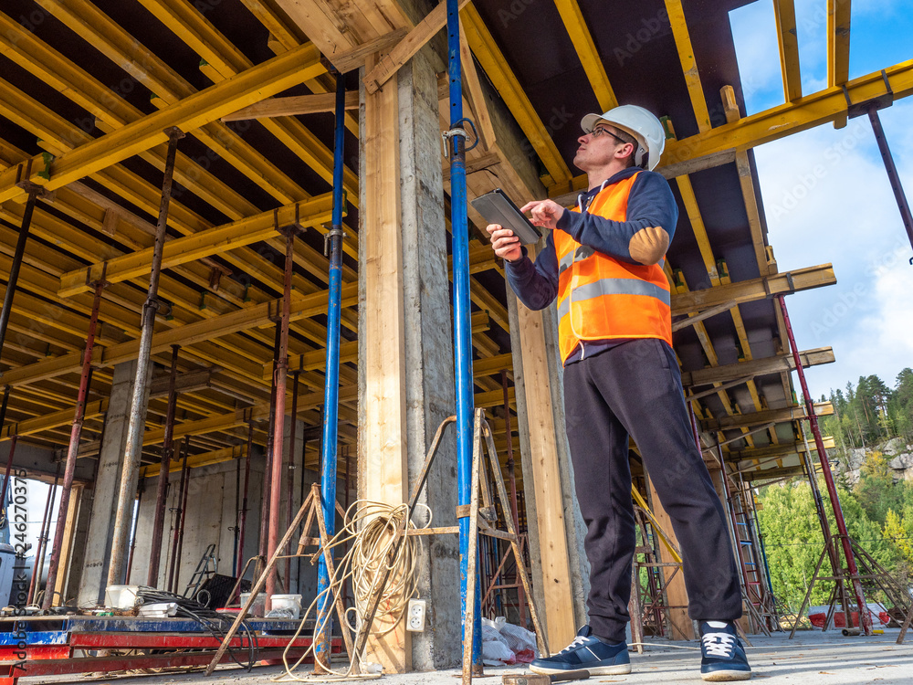 A man in a construction helmet. Verification of construction. A man inspects construction work. The builder inspects the concrete column.