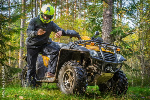 A man travels on ATV. Yellow quad bike. Off-road travel. A man studies the map of the area by phone. Yellow ATV.