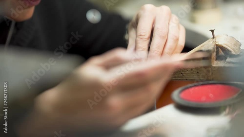 Close scene of working process.  The master is making detail for jewelry with special equipment. There are many other supplies on the background which are lying on the table.