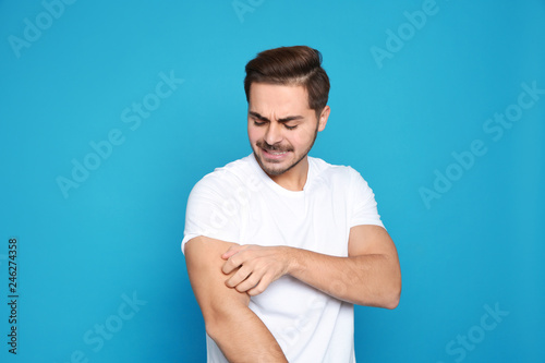 Young man scratching arm on color background. Annoying itch photo