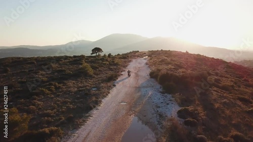 Aerial shot of following a motorcyclist while he drives on gravel road during golden hour on a mountain next to Athens, Greece . photo