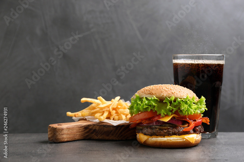 Burger with bacon, soda drink and french fries on table against grey background, space for text