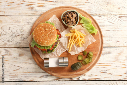 Board with tasty burger, french fries and vegetables on wooden table, top view