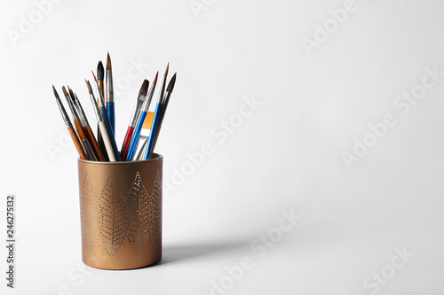 Holder with different paint brushes on white background. Space for text