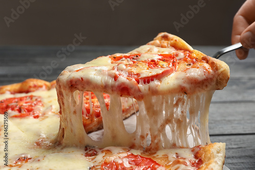 Woman taking slice of hot cheese pizza Margherita on table, closeup
