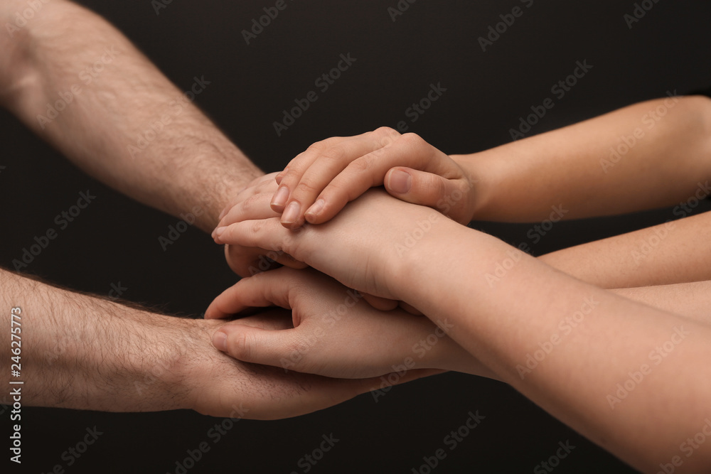 Young people putting their hands together on dark background, closeup