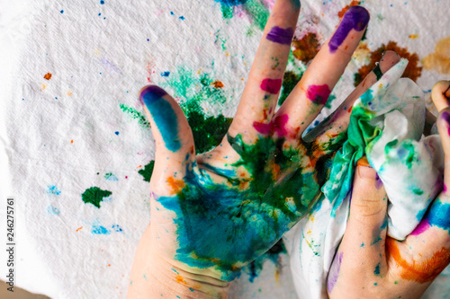  A child cleans up hands that are covered in red, pink, yellow, orange, red, blue, green, and purple ink. Concepts: art, education, play, watercolor, finger painting, mess, creativity, fun, enjoyment