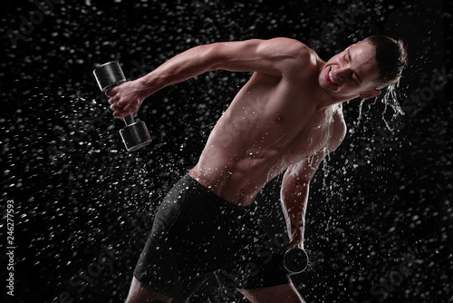 Handsome young man trains with dumbbells with water splashes on his face and chest in Studio shot