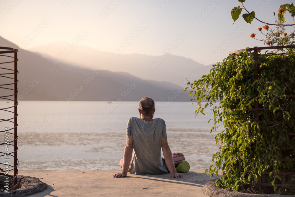 Back of Man Meditating Facing a Calm Lake in Pokhara Nepal at Sunset
