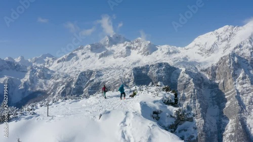 Aerial shot of two hikers on top of the snowy mountain peak, with mountain Triglav in the background, Slovenia