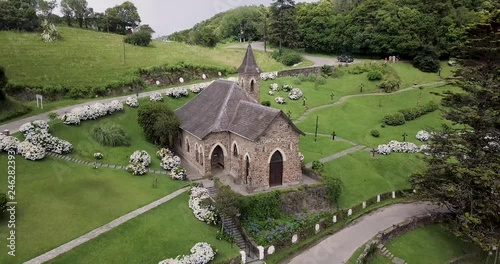 Aerial view crossing roof of Villa Nogues rural little stone church with slate roof, moving closer to tower spire. photo