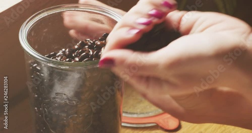 A woman‚Äôs hand pours a jar of coffee beans into her other hand and pulls it out of frame. photo