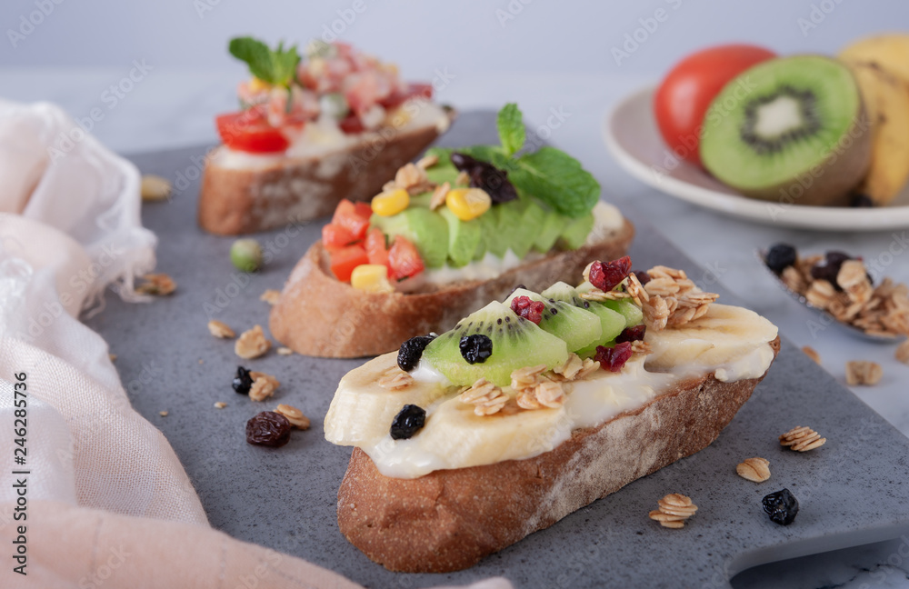 Sandwiches with banana, kiwi, grains and mayonnaise on gray board as background