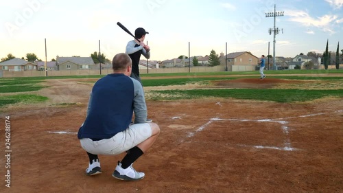 A pitcher throwing a strike in slow motion during an amateur game inning in a public park baseball field during spring time in America.