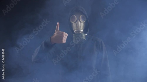 Portrait of Man in Gas Mask and Hood at smoky dark place showing Thumbs up. Approval concept.