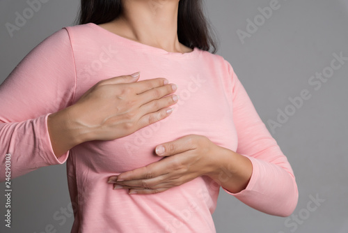 Woman hand checking lumps on her breast for signs of breast cancer on gray background. Healthcare concept. photo