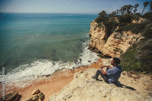 African man seating on beautiful cliff, looking to ocean, enjoy travel holiday. Algarve, Portugal