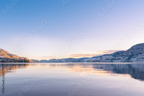 Clear sky with sunset colors reflected in calm lake waters  with view of distant snow covered mountains