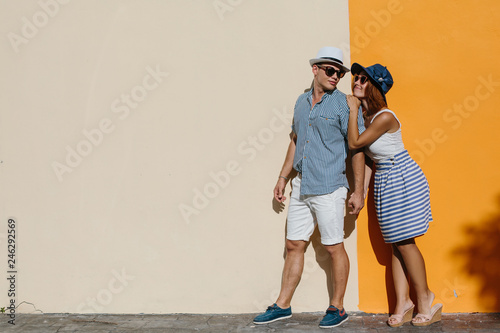 Happy smiling couple near orange sunny wall outdoor. Summer vacation, enjoy holiday