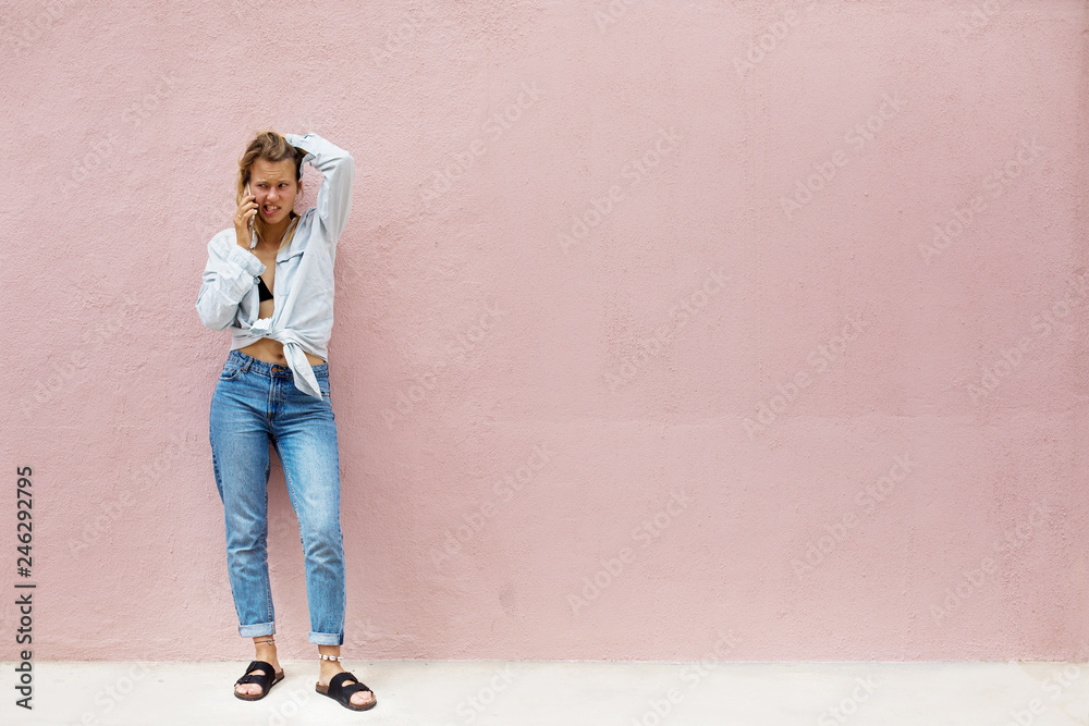 Young sad girl talking by mobile phone, standing outdoor with pink wall on background. Space for text Young sad girl talking by mobile phone, standing outdoor with pink wall on background. Space for text