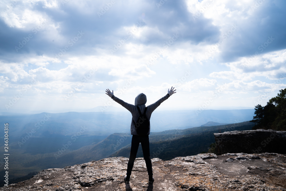 Obraz premium A person hands up standing on rocky mountain looking out at scenic natural view and beautiful blue sky