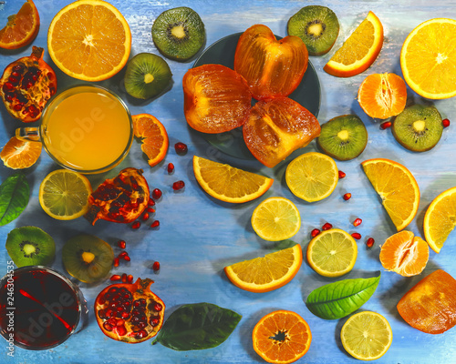 Fototapeta Naklejka Na Ścianę i Meble -  Pomegranate juice and orange juice. sliced ​​citrus fruits on a blue painted board. orange, kiwi, pomegranate, persimmon, mandarin.