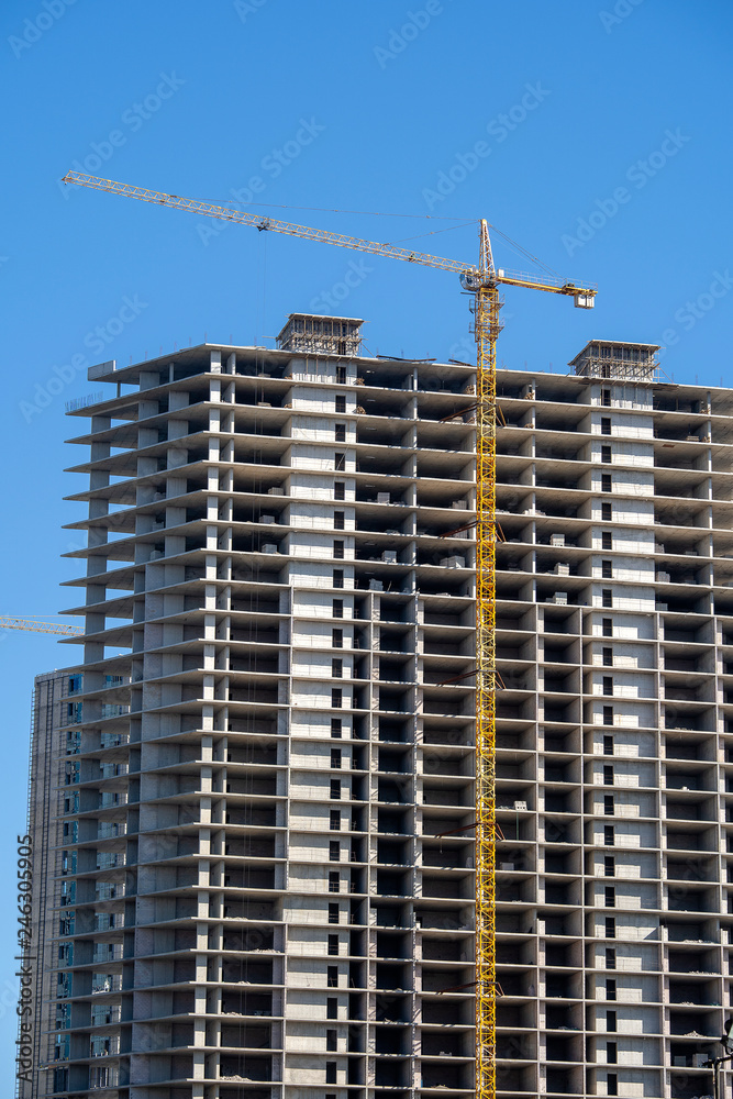 Construction of a high-rise building with a crane. The construction crane and the building against the blue sky.