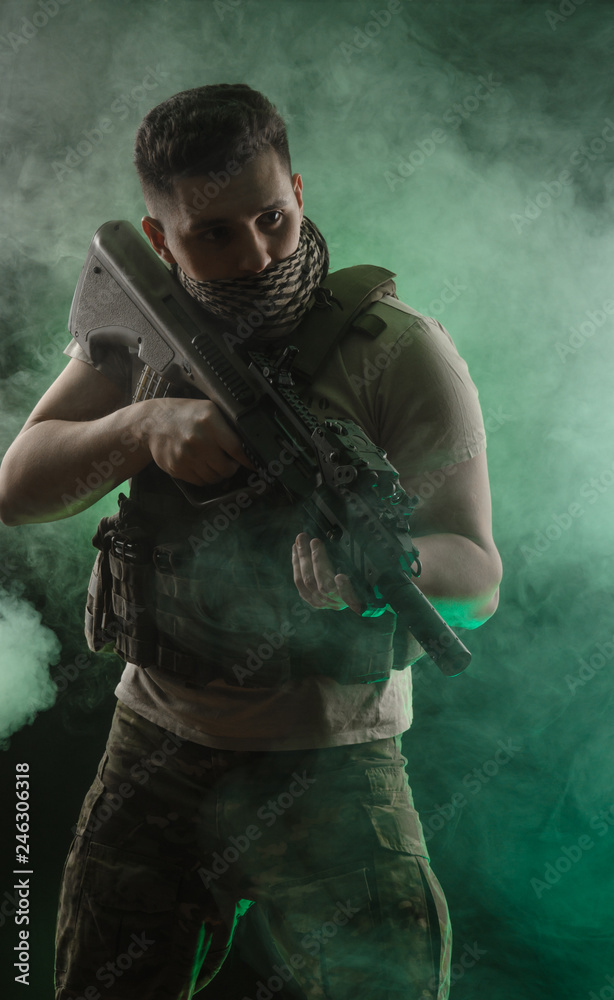 the man in military special clothes posing with a gun in his hands on a dark background in the haze