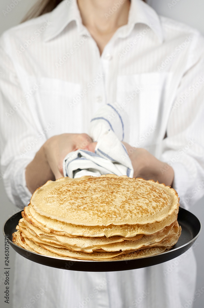Stack of russian pancake blini in pan woman holds in hands
