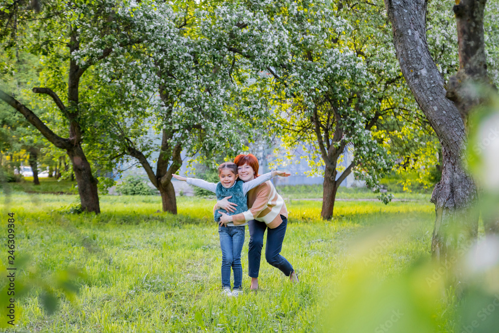 Fototapeta premium Mother and daughter having fun near blossom apple trees