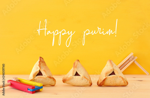 Purim celebration concept (jewish carnival holiday). Traditional hamantaschen cookies over wooden table and yellow background.