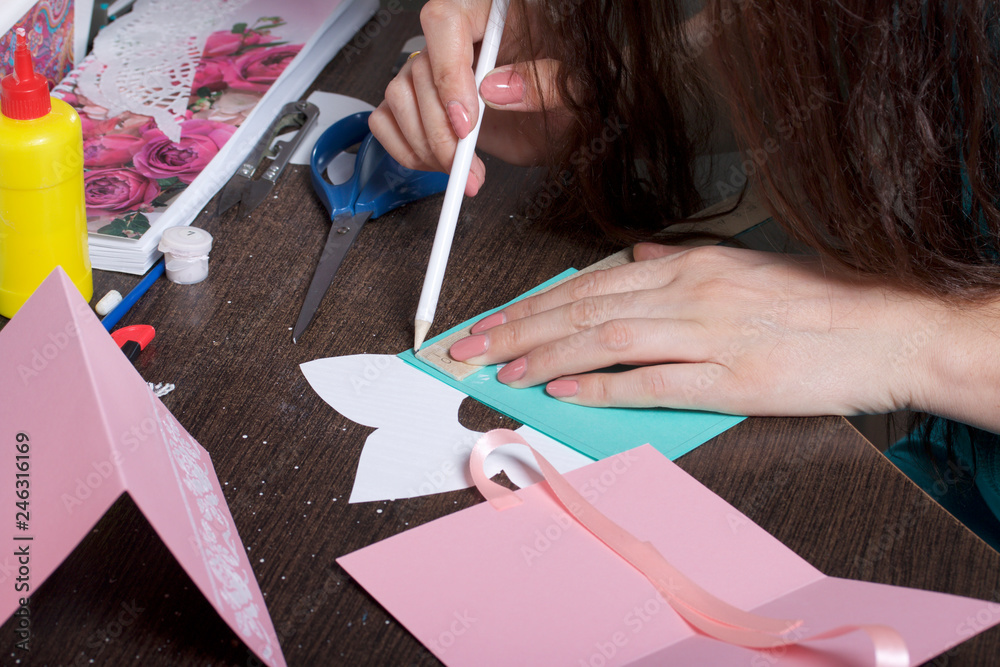 Fototapeta premium Making greeting cards from paper, cardboard and tape. Woman artisan makes a markup with a pencil.
