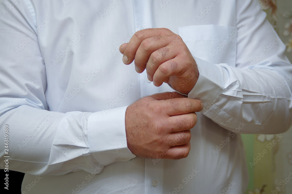 The man fastens the cuffs of the shirt. Morning of the groom