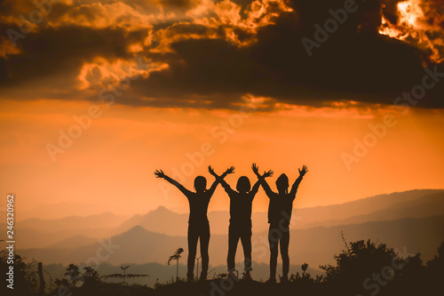 The silhouette of a woman standing watching the sunset sky Darling pointed to the cloud Colorful sky, orange sky and golden sky Queue of close friends © EKKAPON