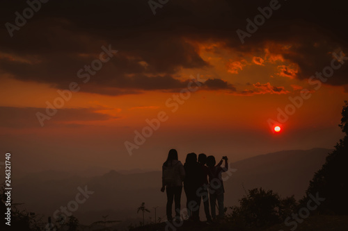 The silhouette of a woman standing watching the sunset sky Darling pointed to the cloud Colorful sky, orange sky and golden sky Queue of close friends