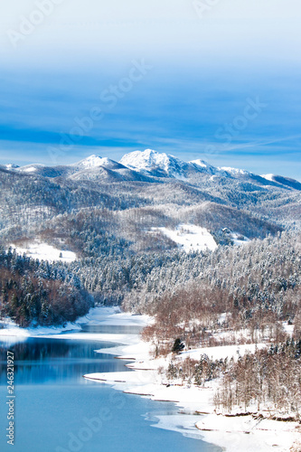  Croatian nature landscape, beautiful winter panorama of Lokvarsko lake and woods under snow in Gorski kotar and Risnjak mountain in background 